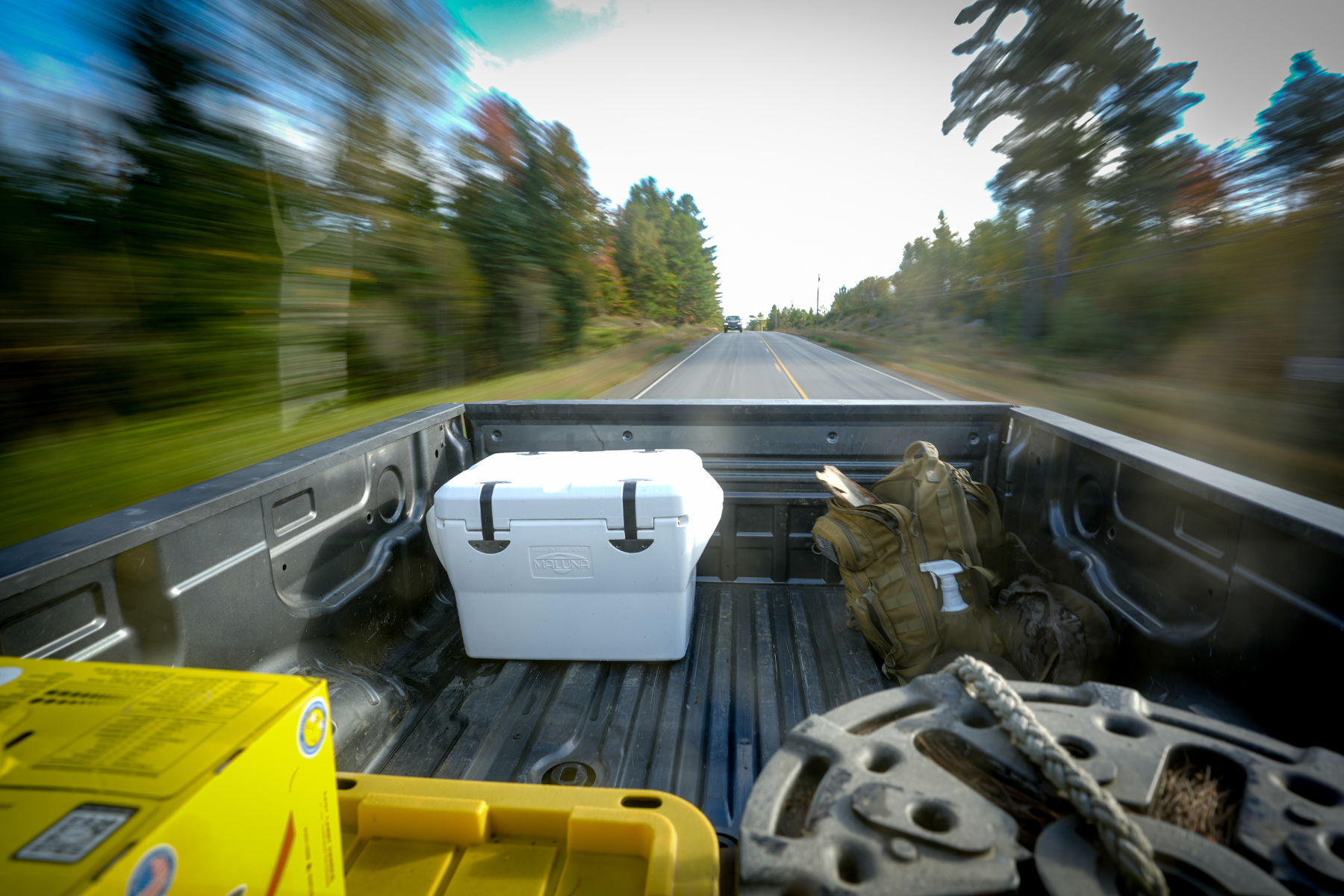 This image takes you to the DUHA Cooler Collection. It shows the bed of a truck, the back of a white cooler, as the background is blurry from driving down a highway.