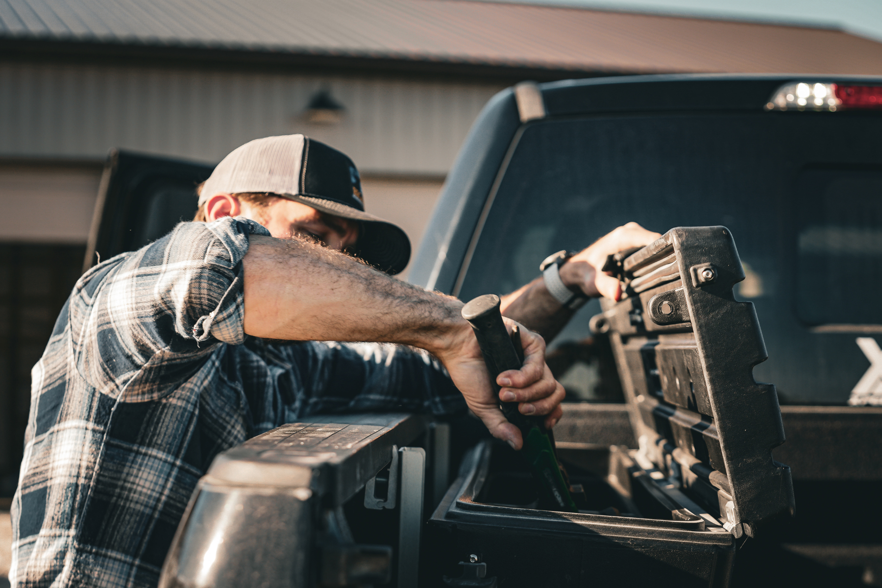 Image block that is linked to the Side Tool Box collection page. Shows a man reaching over the edge of his truck bed into the box to grab a hammer.